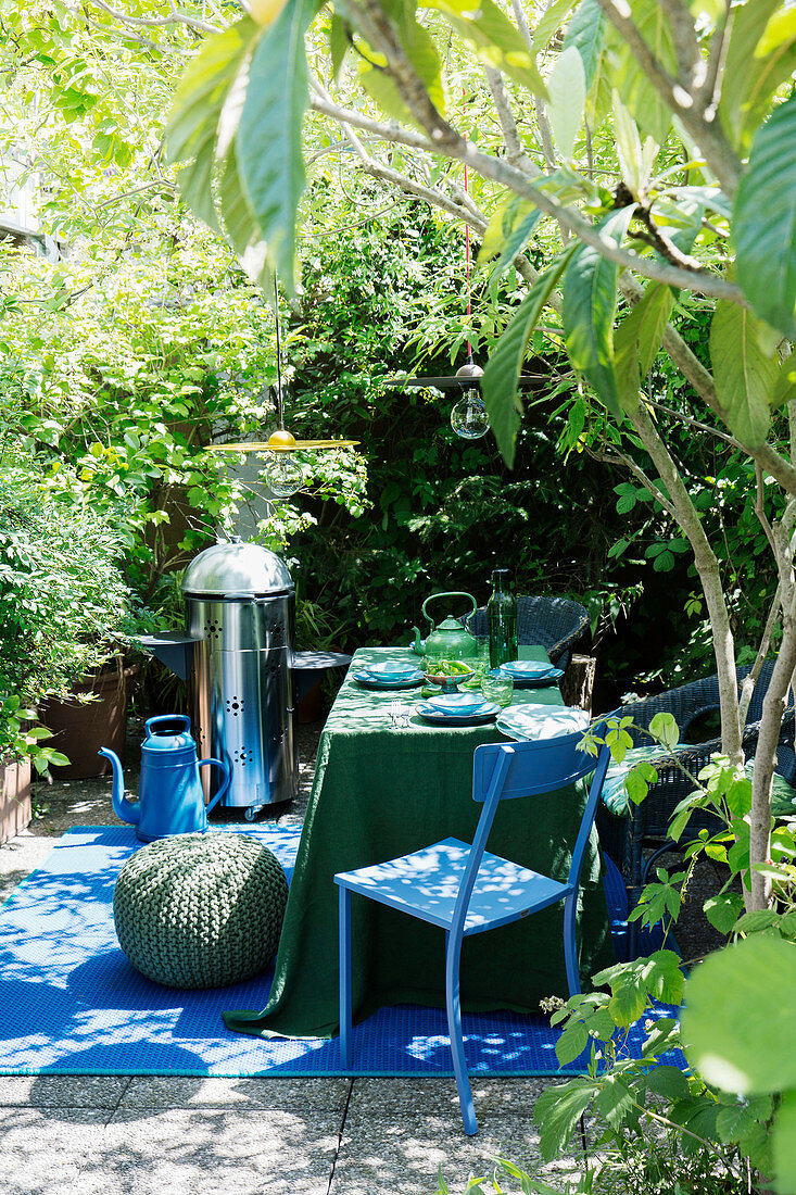 Grill und gedeckter Tisch in Grün und Blau auf sommerlicher Terrasse