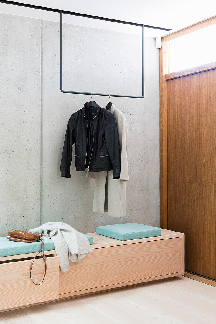 Bench and minimalist coat rack in hallway with concrete wall