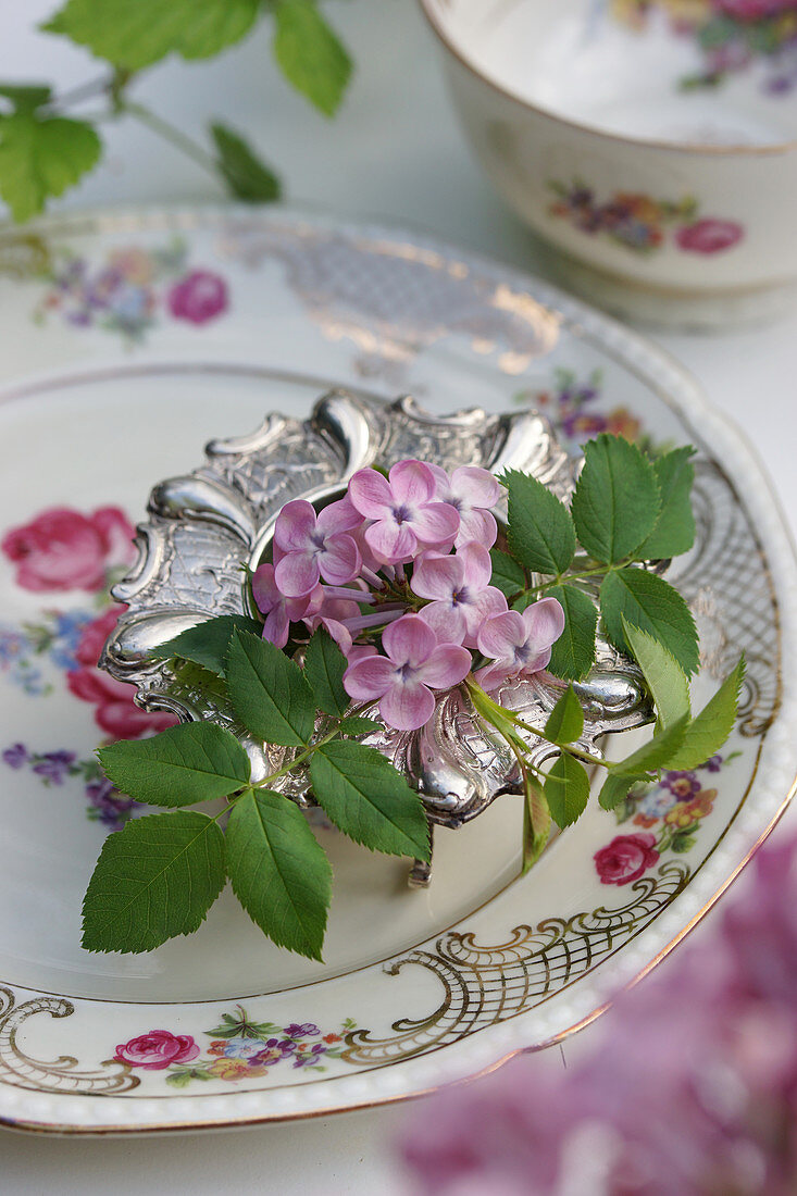 Fliederblüte und Rosenblätter in silbernem Eierbecher