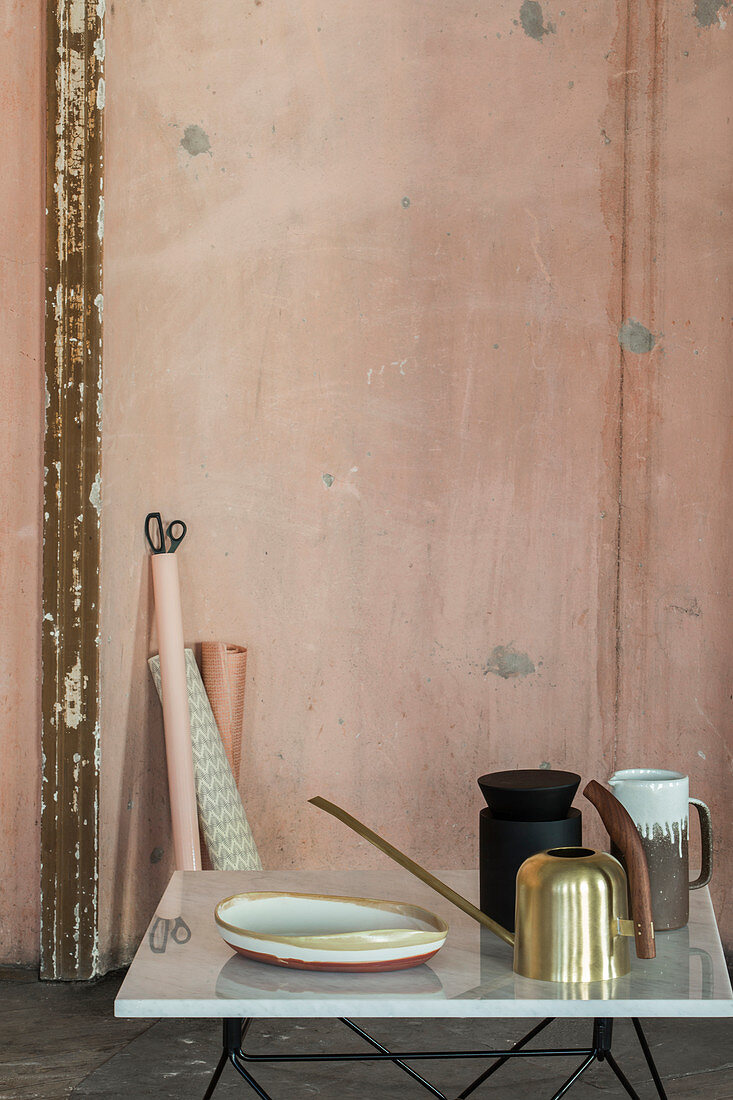 Golden watering can and ornaments in front of battered pink wall