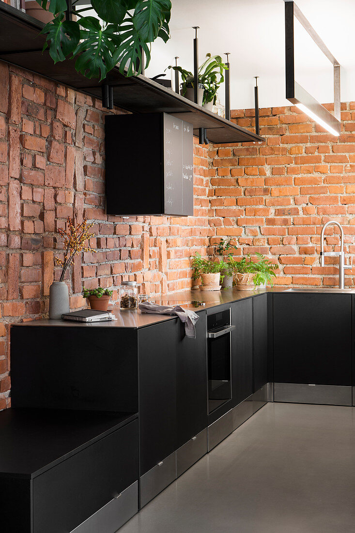 Black kitchen cabinets with plinth drawers against exposed brick walls