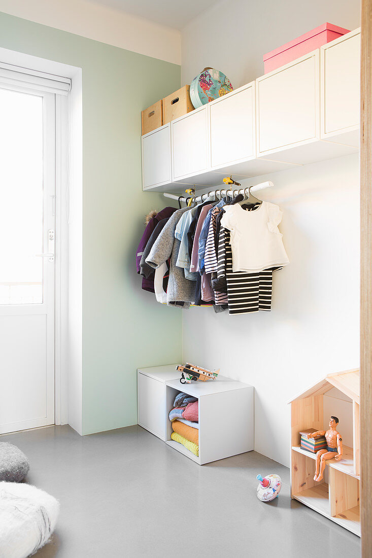 Wall-mounted cupboards and clothes rail in simple child's bedroom