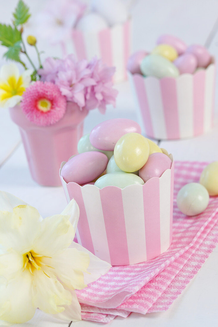 Sugar eggs in paper cupcake holders next to narcissus flower