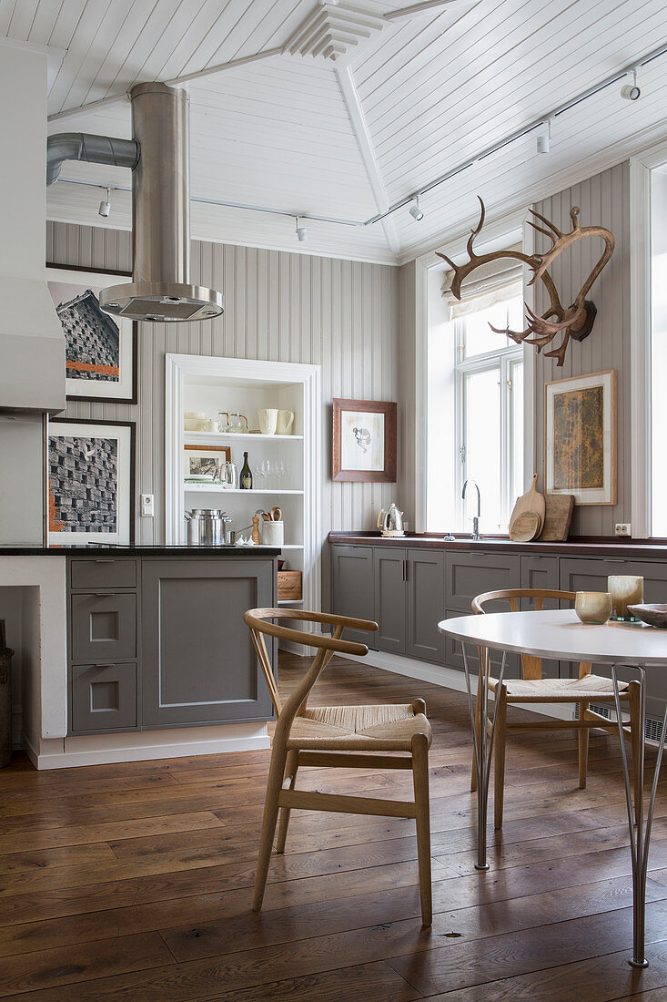 Designer chairs at dining table in front of country-house-style open-plan kitchen