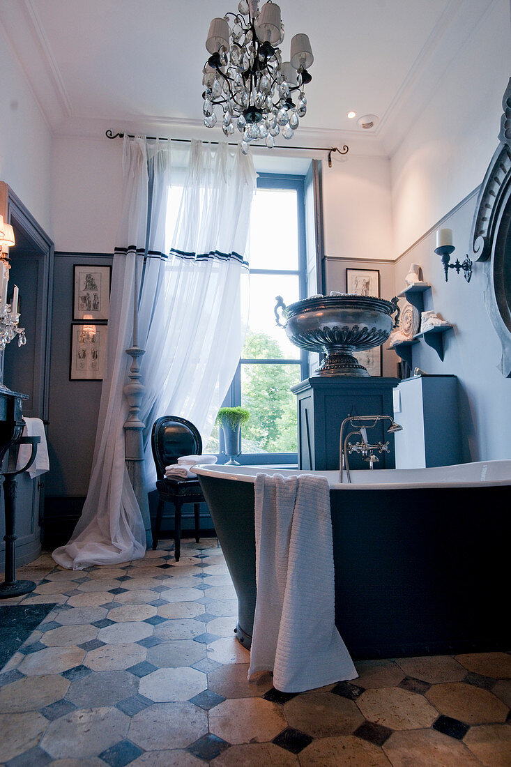 Free-standing bathtub, urn on plinth and chandelier in antique-style bathroom