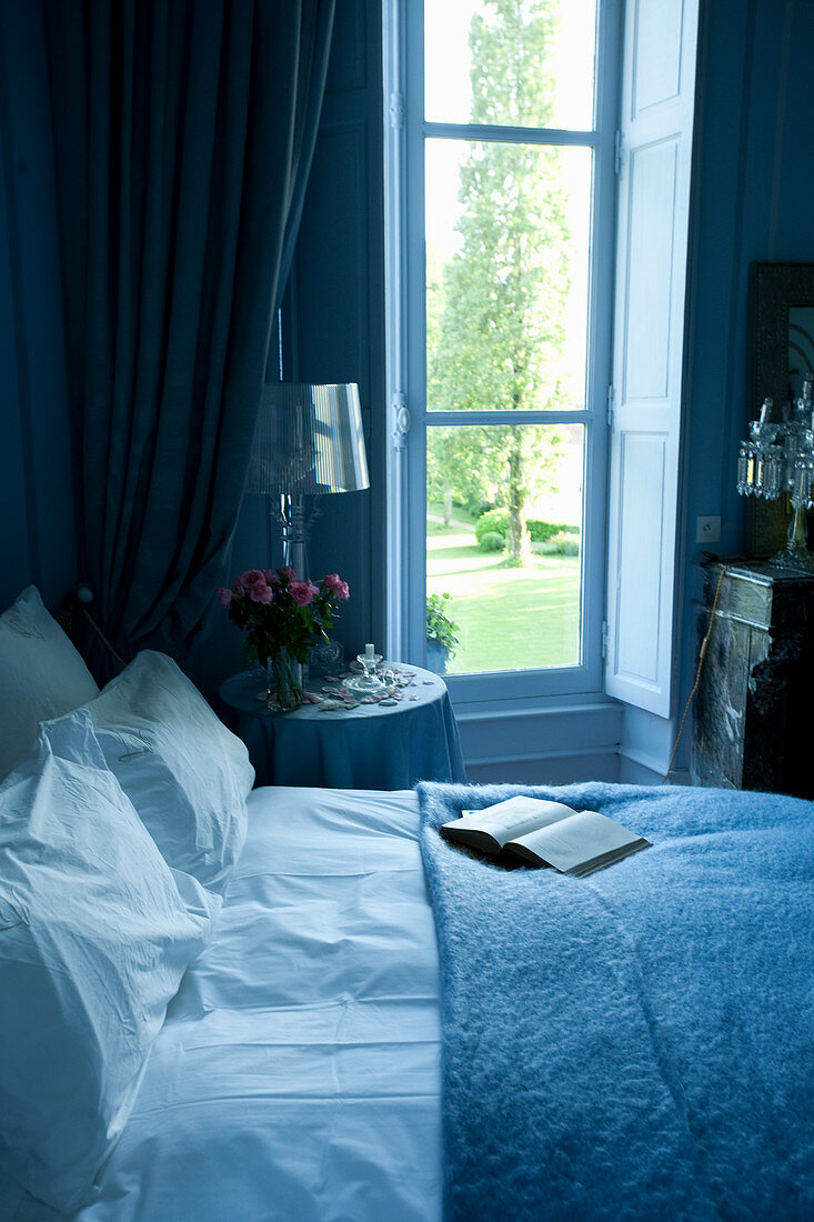 Bett mit Beistelltischchen am Fenster in blauem Schlafzimmer
