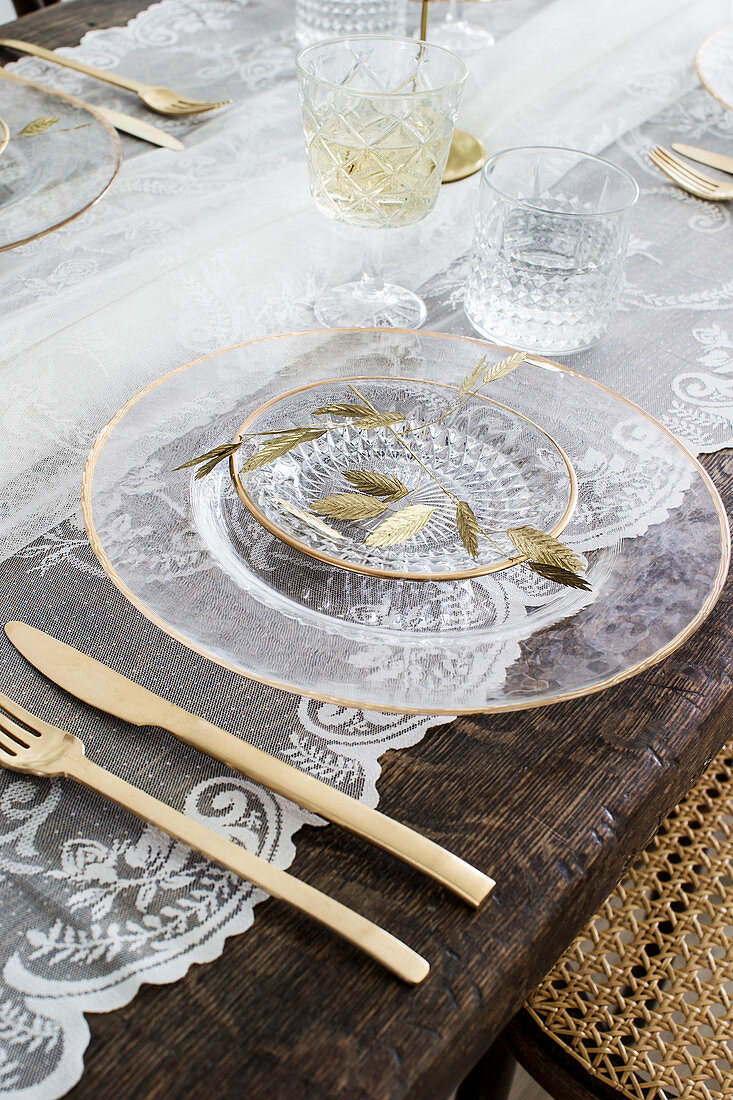 Table set with glass plates, golden cutlery and lace tablecloth