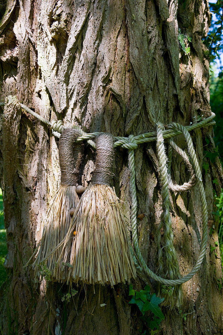 Stroh-Quasten um knorrigen Baum gewickelt als Gartendekoration