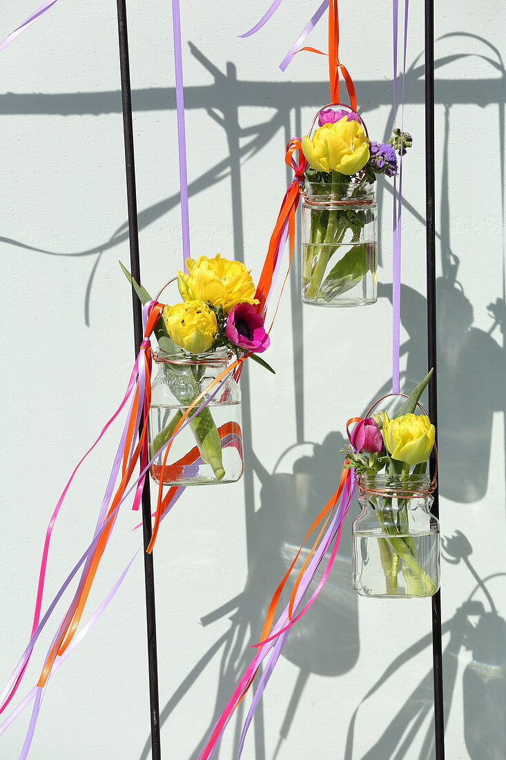 Hängende Schraubgläser mit Blumen und bunten Stoffbändern