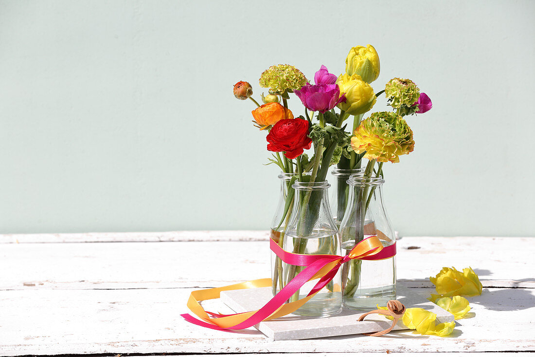 Colourful spring flowers in four glass bottles tied with ribbon