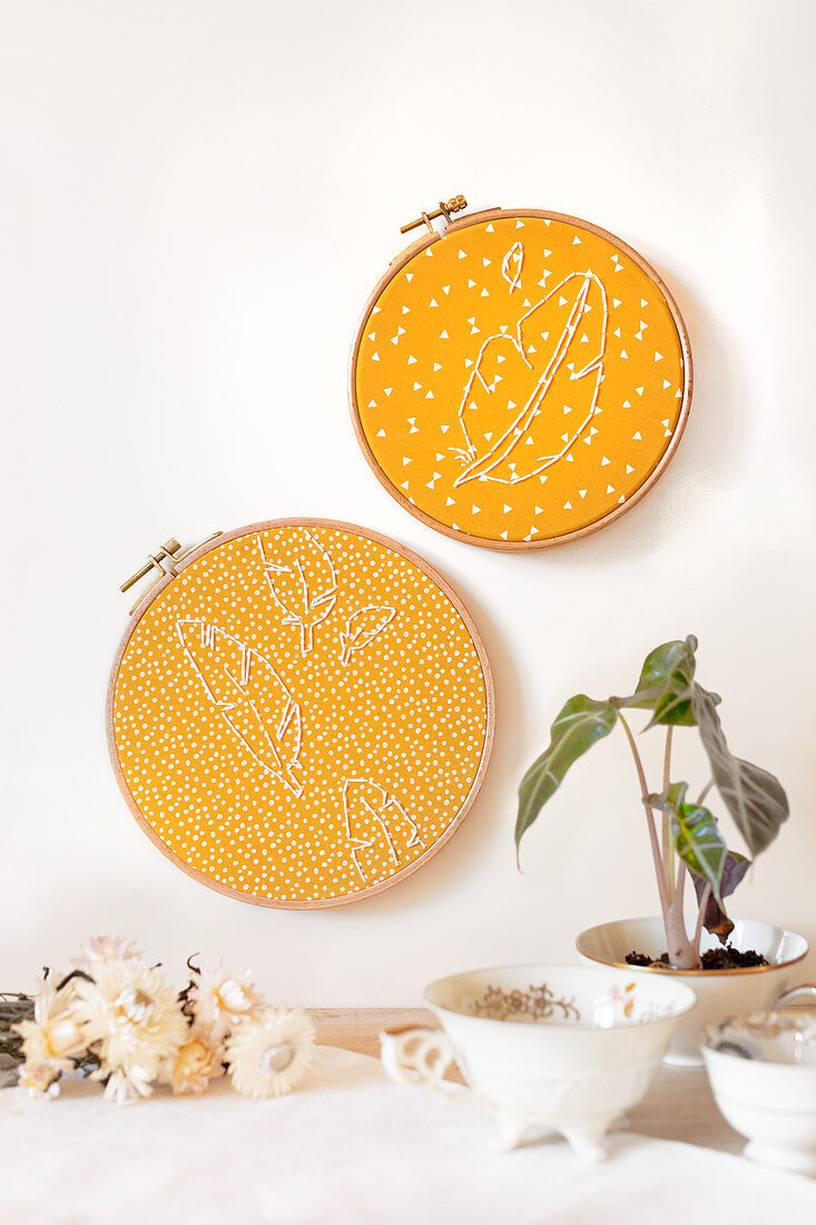 Feathers embroidered on yellow patterned fabric in embroidery frames decorating wall