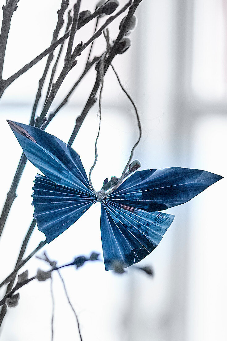 Blue folded paper butterfly hung from willow branch