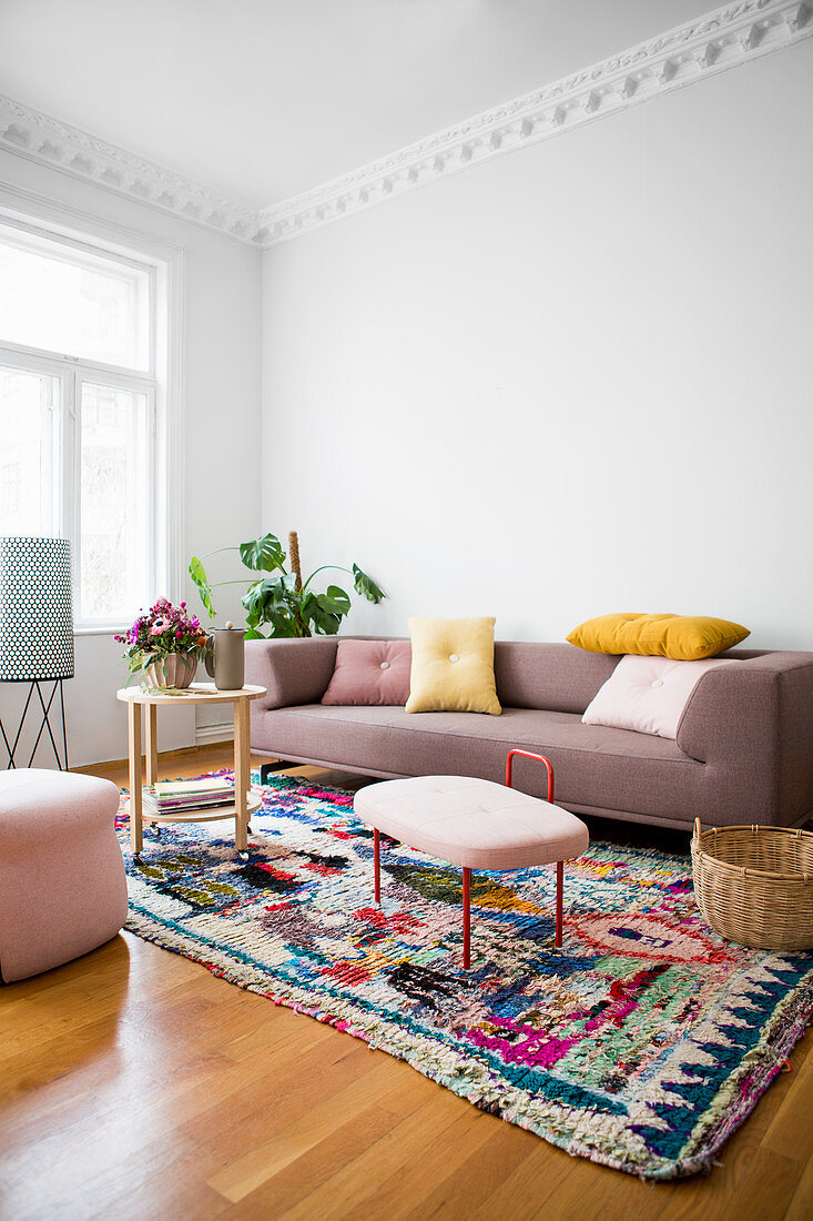 Sofa mit Kissen, Zimmerpflanze und Beistelltische auf buntem Teppich