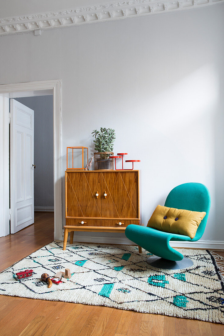 Sideboard und türkisfarbener Designerstuhl auf Berberteppich
