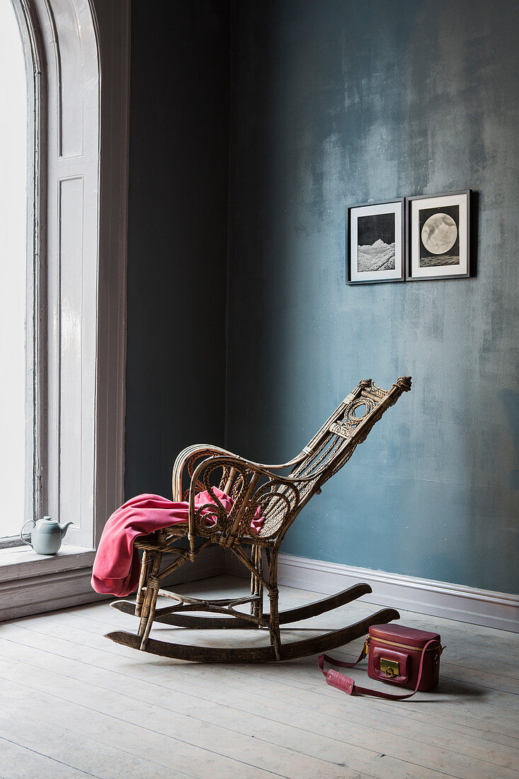 Rocking chair against dark blue wall and next to large arched window