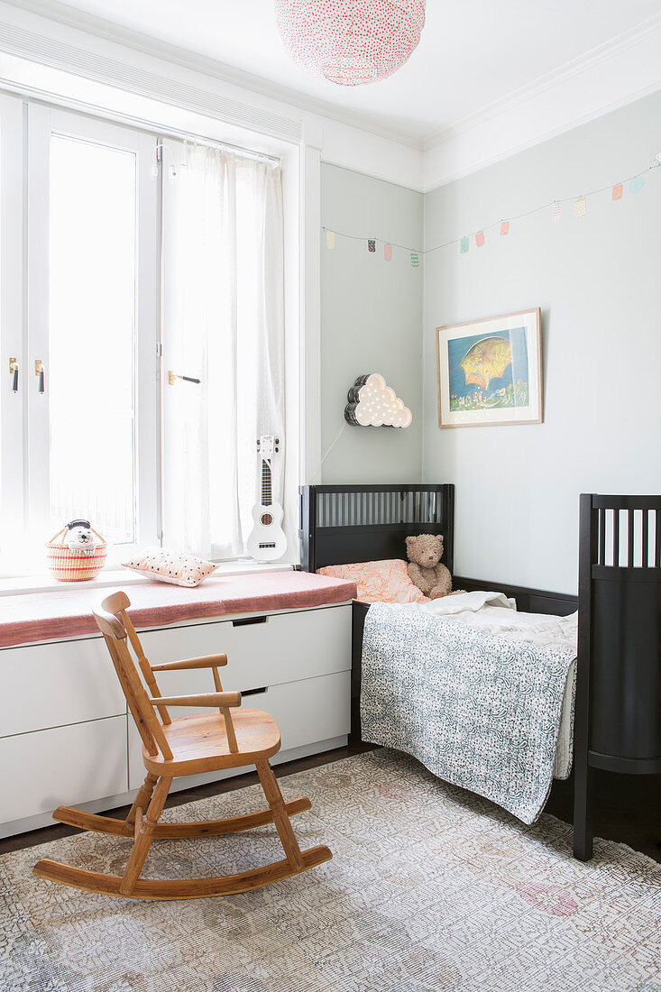 Rocking chair next to window seat with chest of drawers below in child's bedroom