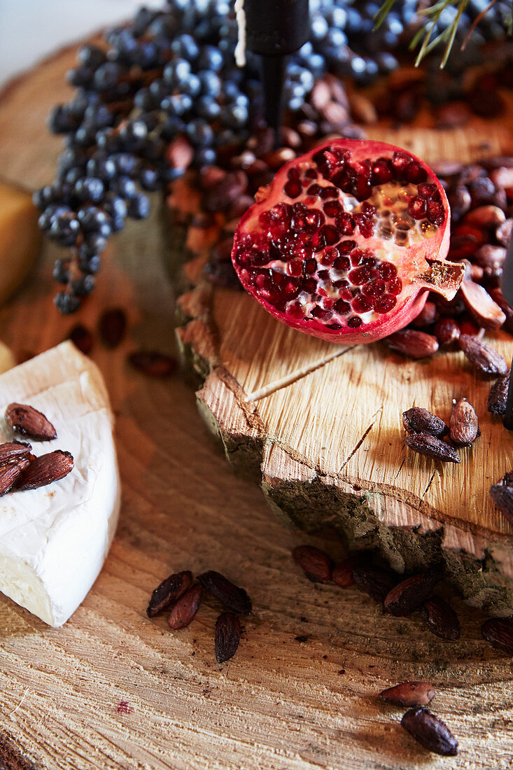 Halved pomegranate, roasted almonds and cheese on wooden board