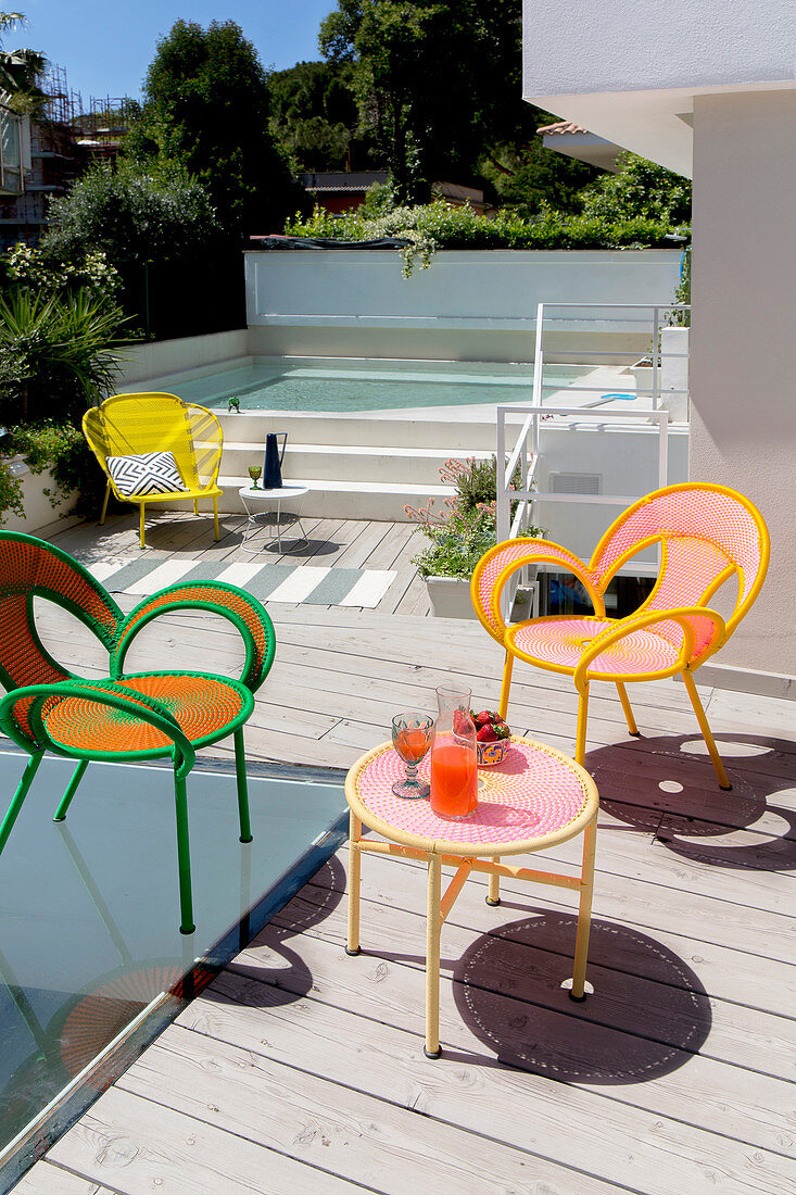 Terrasse mit bunten Stühlen und Tisch, im Hintergrund Pool
