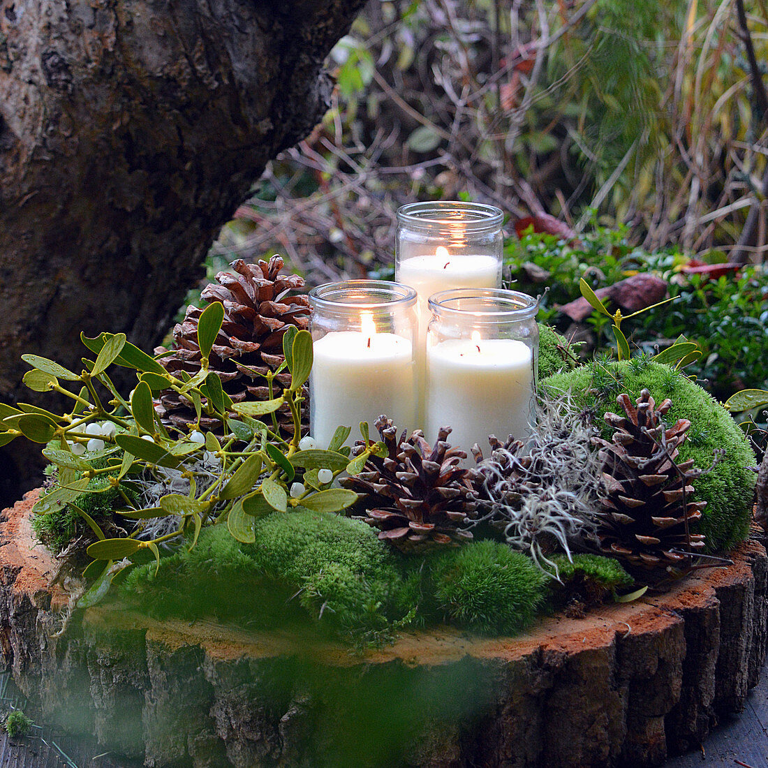 Winterliche Kerzendekoration mit Zapfen, Moos und Mistelzweig auf Holzscheibe