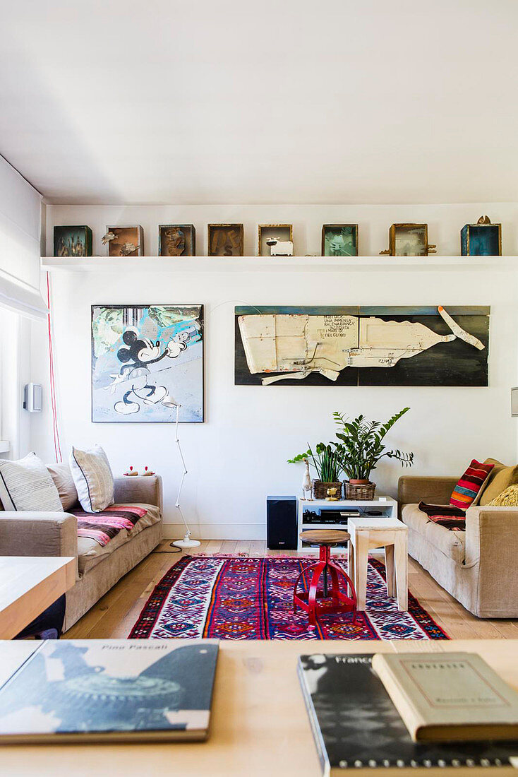 Wohnzimmer mit Leinensofas und Kelim-Teppich darüber Wandbilder mit Wal- und Comicmotiv