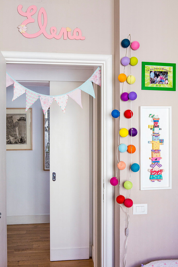 Kinderzimmer mit taubengrauen Wänden, Wimpelkette und farbenfroher Lichterkette als Türdeko
