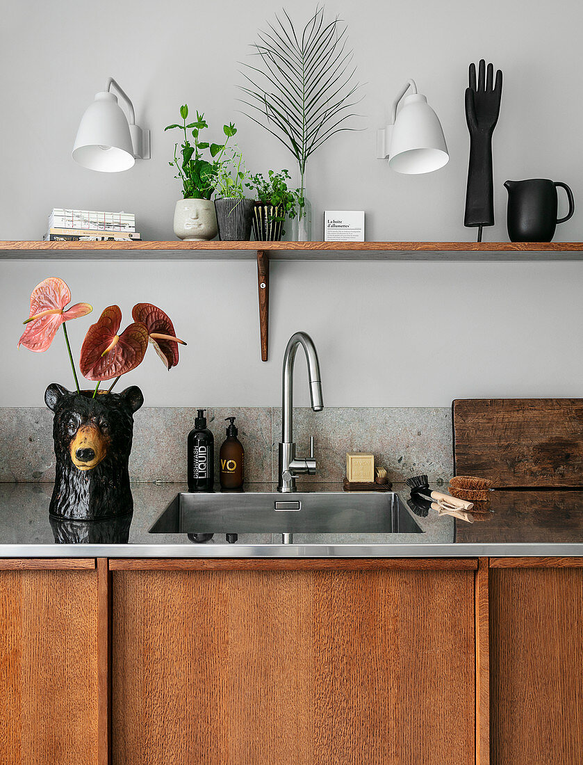 Flamingo flowers in bear-shaped vase next to sink in simple kitchen