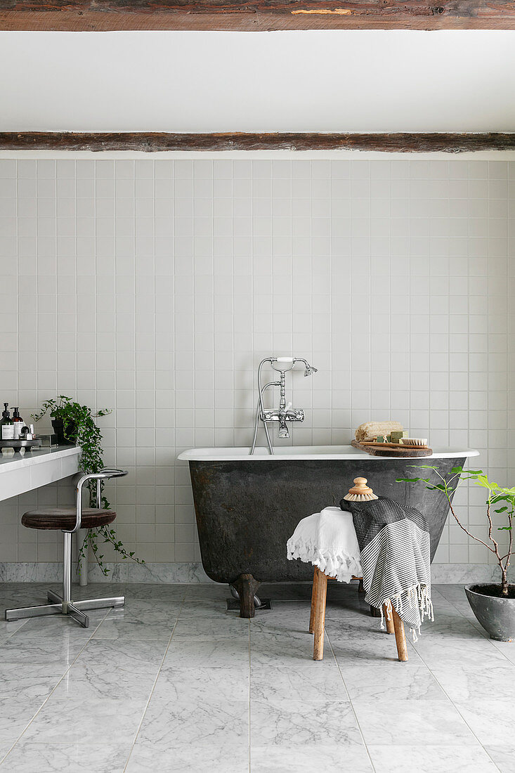 Small, free-standing bathtub in simple bathroom in grey and white