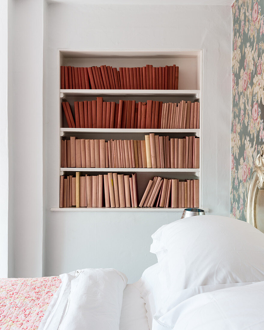 Bücher mit Einbänden in Rottönen im Wandregal im Schlafzimmer
