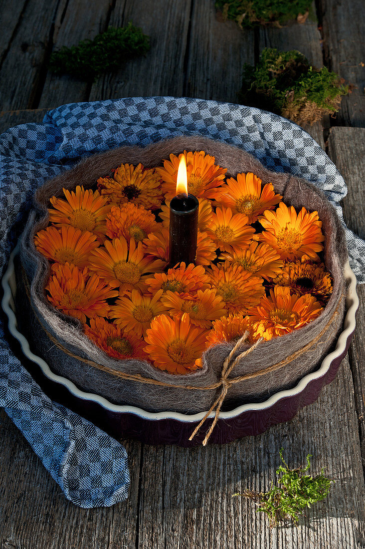 Brennende Kerzen und Ringelblumenblüten in Tarteform mit Filz umwickelt