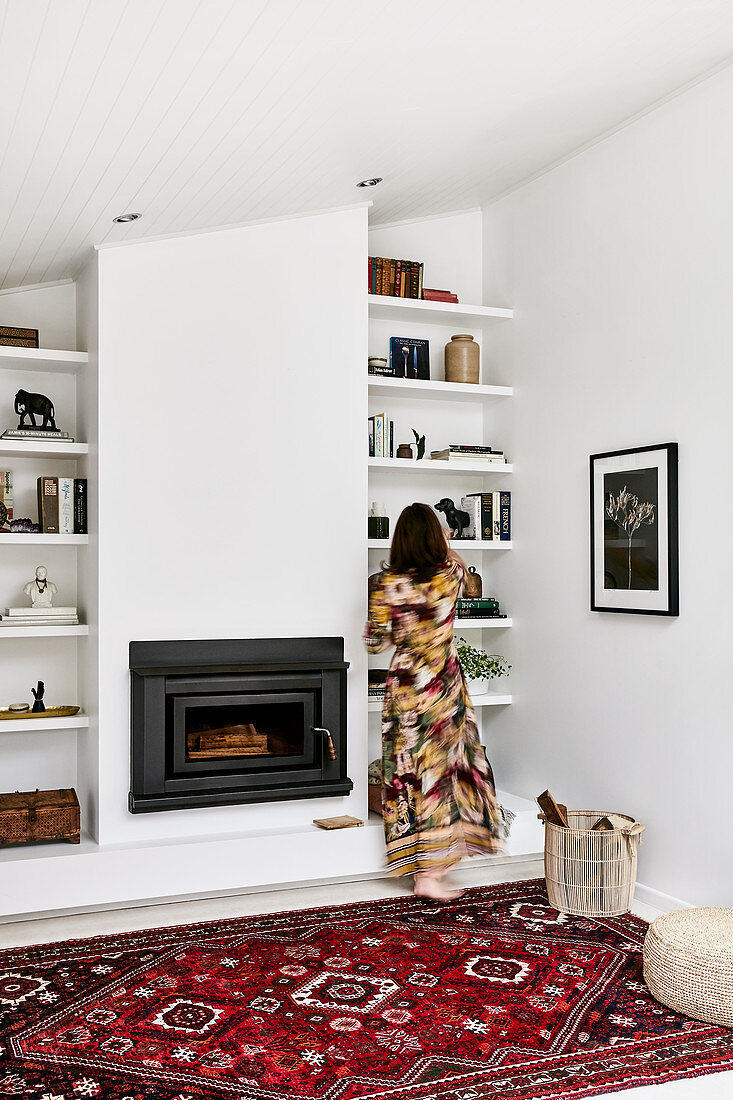 Woman standing in front of shelves next to fireplace in living room