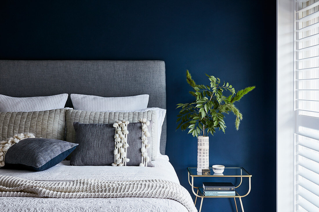 Double bed with grey headboard against petrol-blue wall