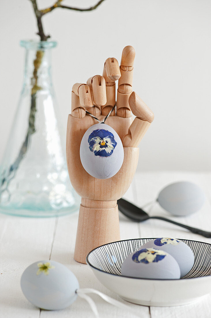 Easter eggs decorated with pressed violas, one hanging from wooden mannequin hand