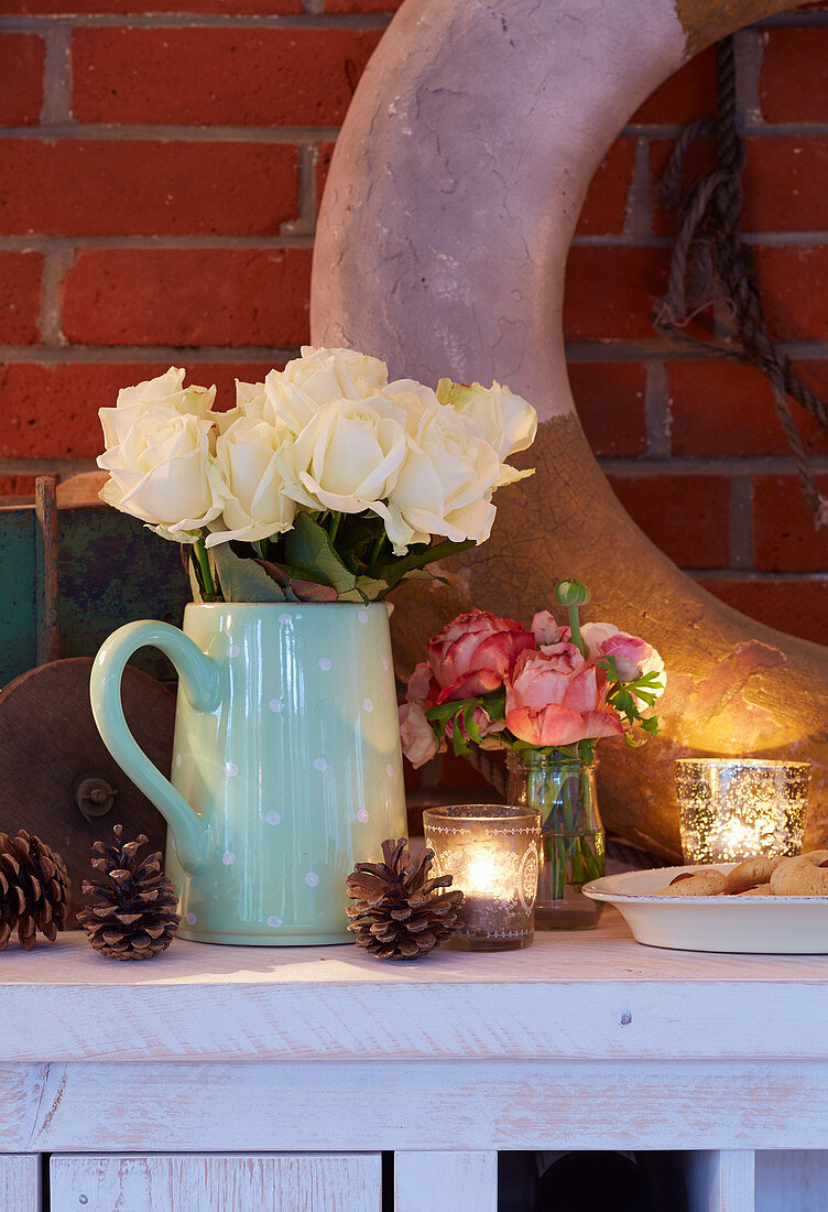 Pine cones, tealights in glass holders and jug of white roses decorating sideboard