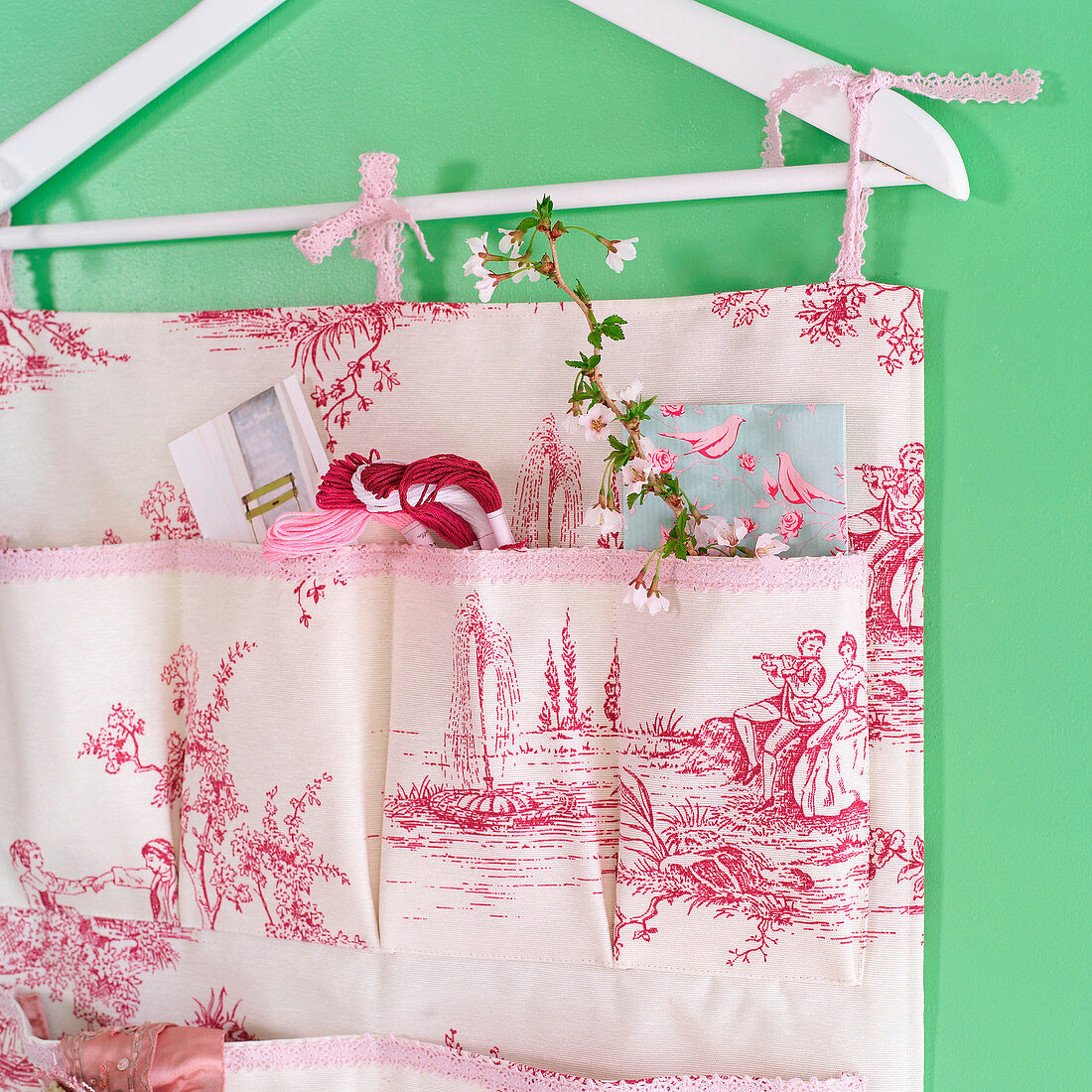 Hand-sewn organiser made from toile-de-jouy fabric hanging from clothes hanger
