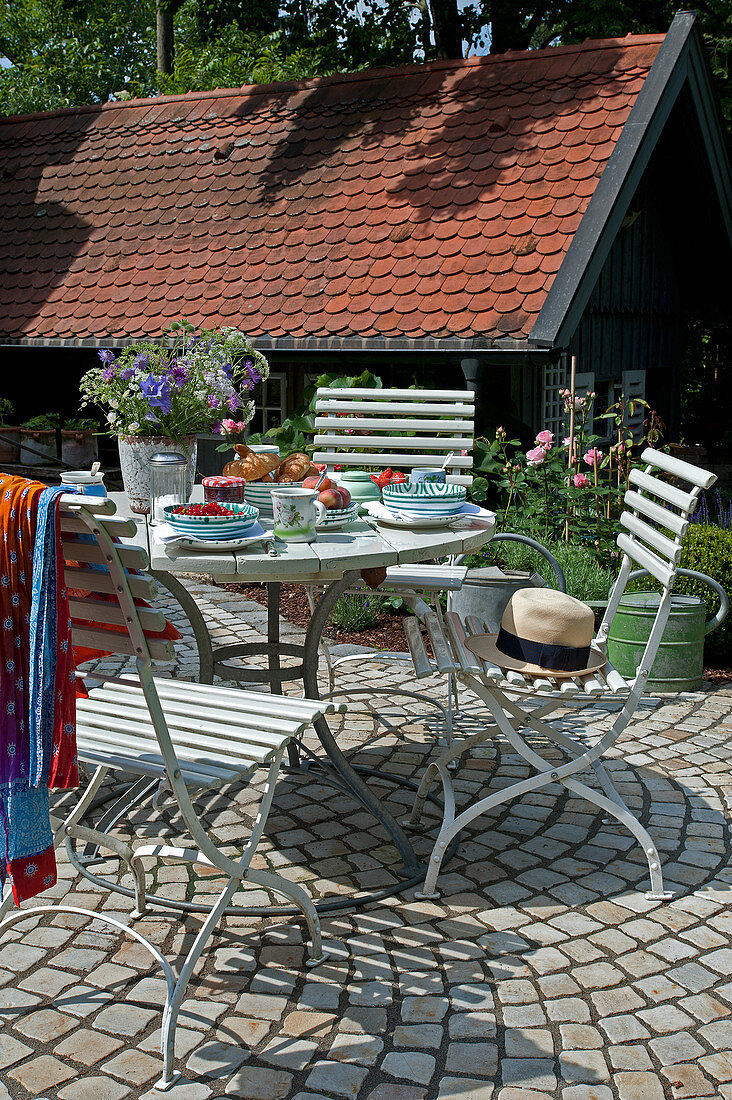 Gedeckter Gartentisch auf gepflasterter Terrasse im Sommer
