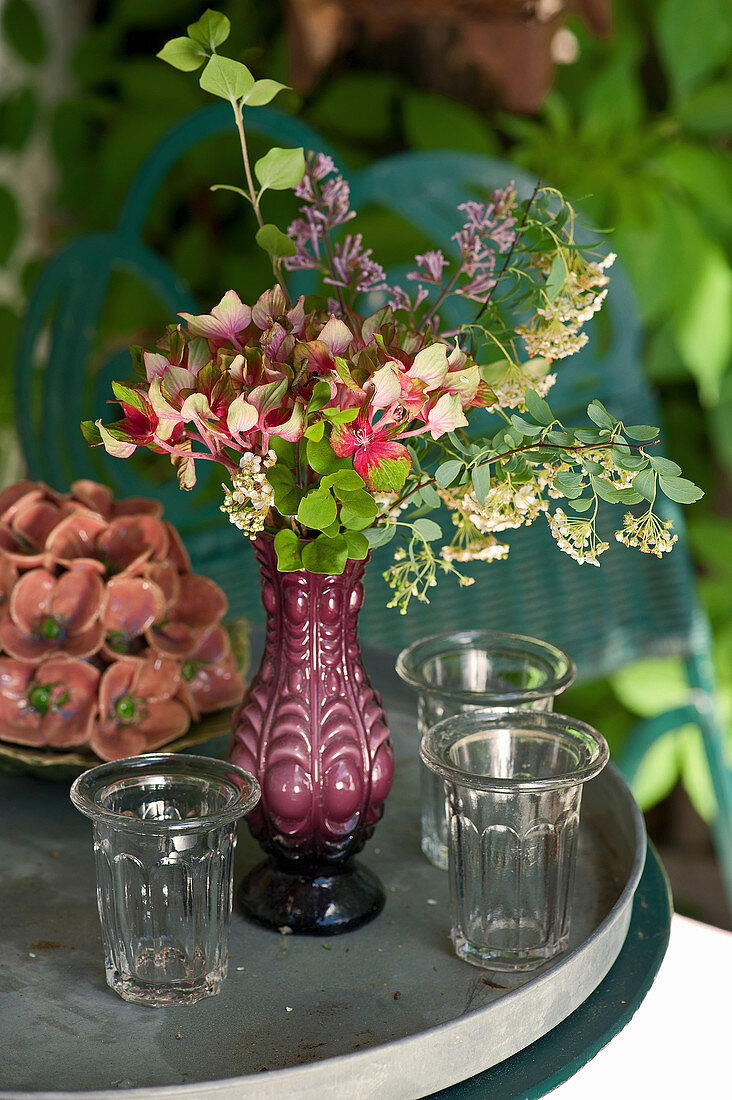 Gläser und Vase mit Blumen auf Gartentisch
