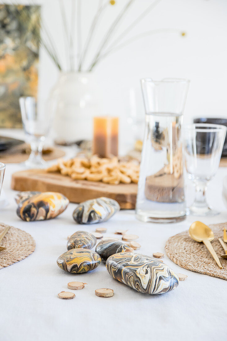 Mit Pouring in Naturtönen bemalte Kieselsteine auf gedecktem Tisch