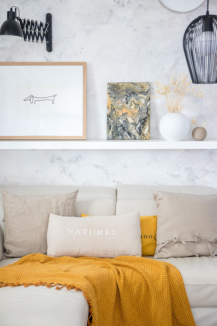 Picture painted with marble pour technique on shelf above sofa with beige and ochre cushions