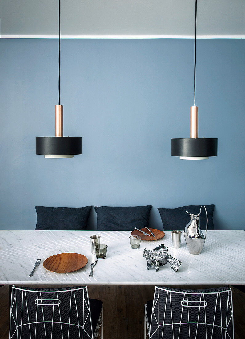 Designer lamps above dining table in front of pale blue wall