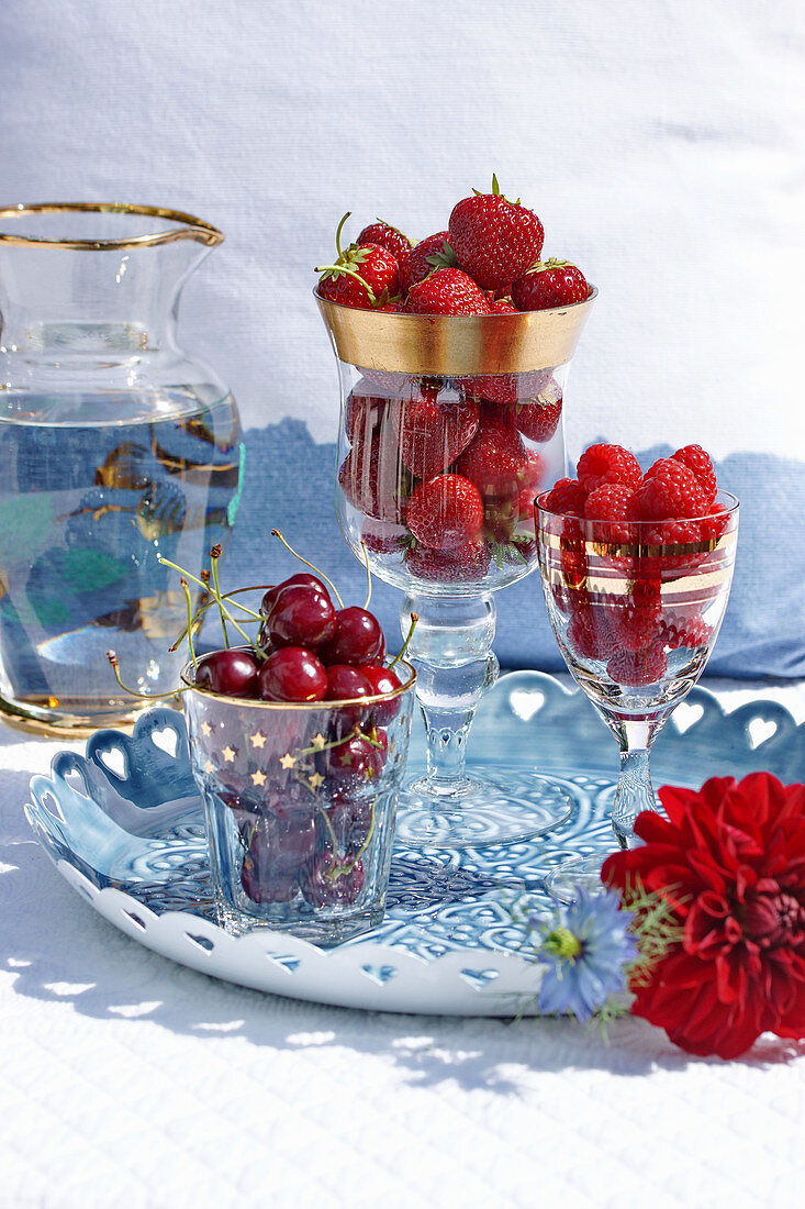Glasses with sweet cherries, strawberries and raspberries on a tray