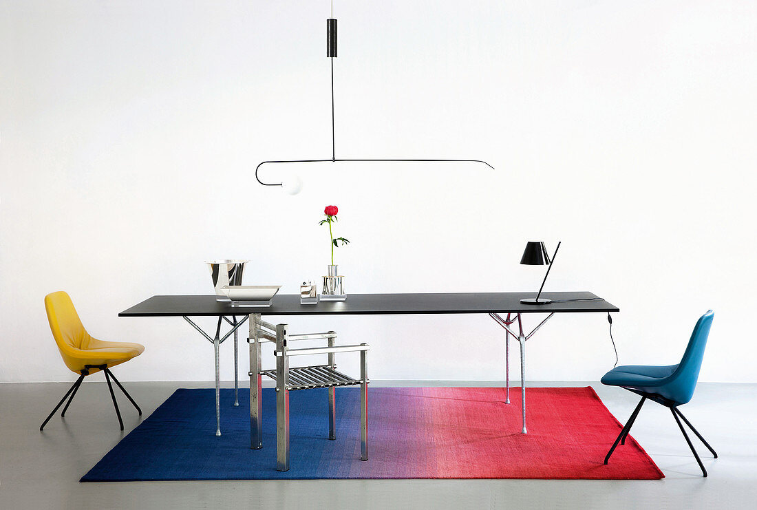Schwarzer Metalltisch mit verschiedenen Designerstühlen auf Farbverlauf-Teppich