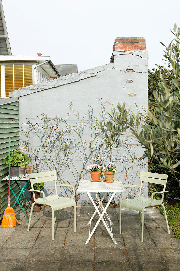 Grüne Gartenstühle am Klapptisch auf der Terrasse vor einer Hauswand