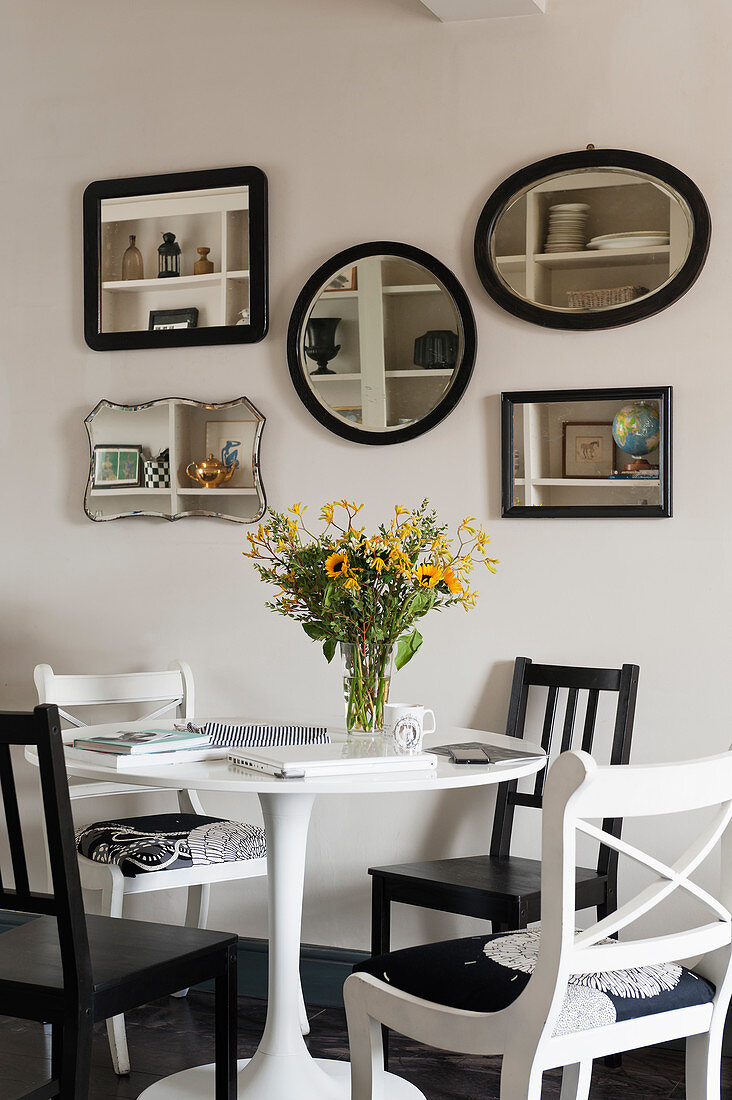 Arrangement of mirrors on wall above dining table and various chairs