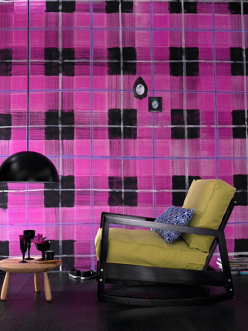 Armchair and side table in front of wall with wallpaper in oversized pink-and-black tartan pattern