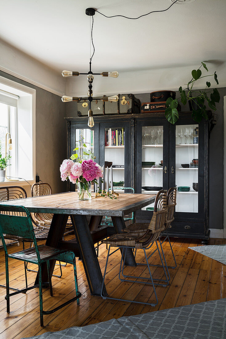 Dining table with rustic wooden top and vintage chairs in front of glass-fronted cabinet
