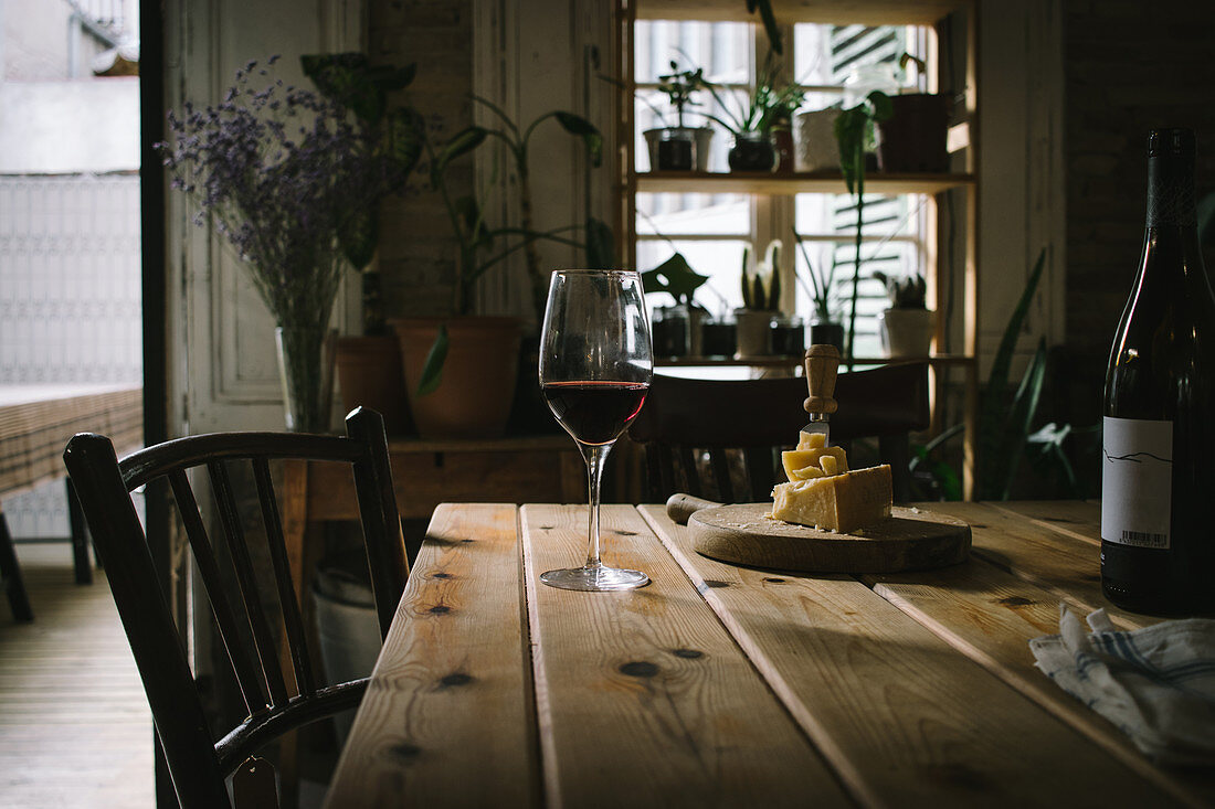 Rotweinflasche und -glas mit Käseplatte auf rustikalem Holztisch
