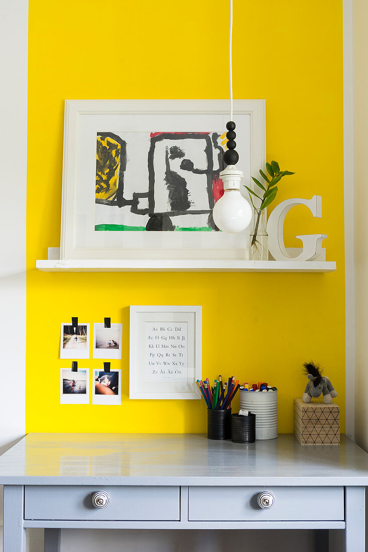 Regalbrett an gelber Wand überm grauen Schreibtisch