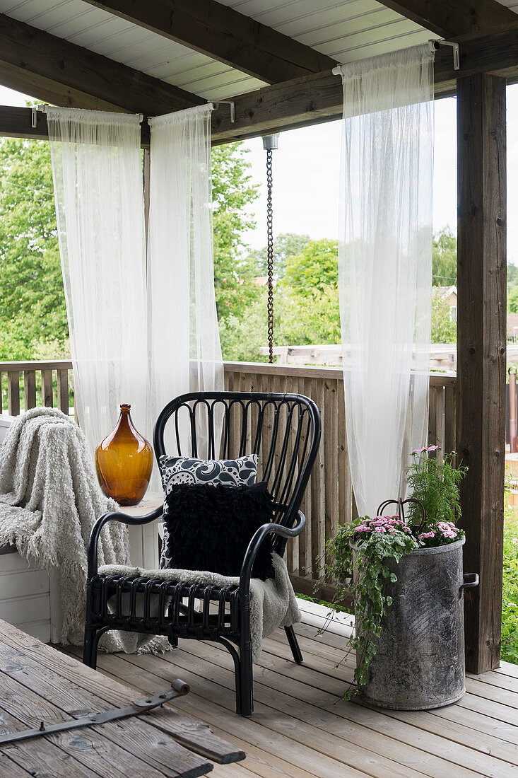 Black rattan chair on roofed terrace with curtains
