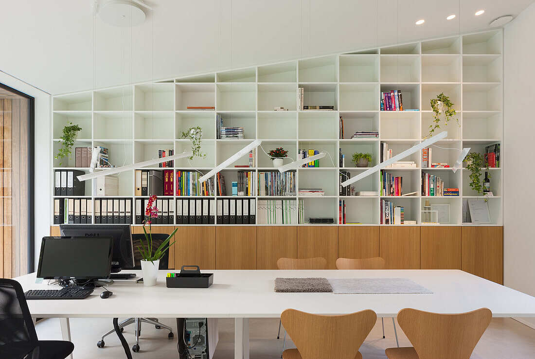 Modernes Arbeitszimmer mit großem Bücherregal, hölzernem Sideboard und weißem Schreibtisch