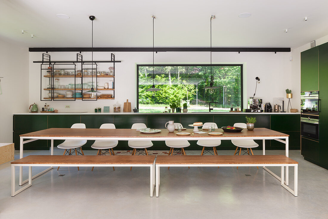 Langer Esstisch mit Bänken und Stühlen vor dunkelgrüner Küchenzeile